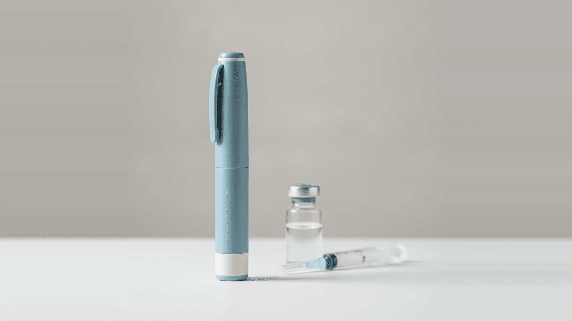 A GLP-1 injection pen standing beside a glass vial and a syringe on a clean surface — representing the semaglutide and tirzepatide products at the center of the 2024–2026 compounding and regulatory changes.